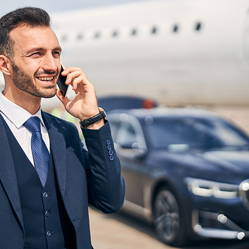A man awaits airport limo transportation while he stands next to a plane.
